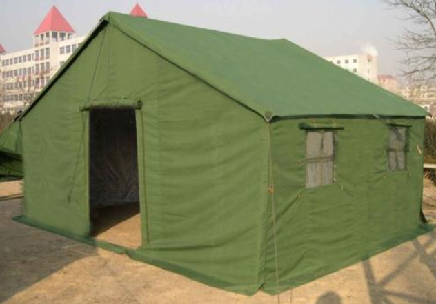 A green canvas tent set up outdoors with buildings and bare trees in the background, muted daylight scene